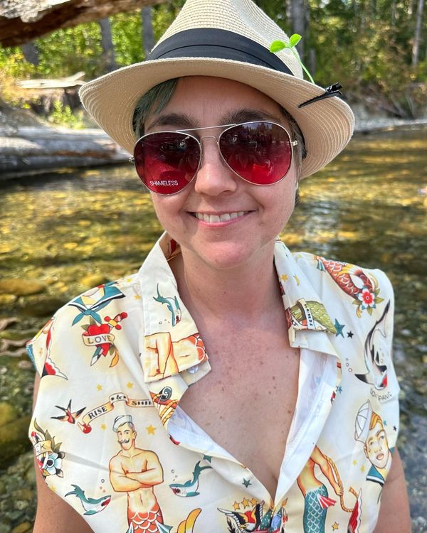 Jen Woolfe smiling in a straw hat and red sunglasses outdoors
