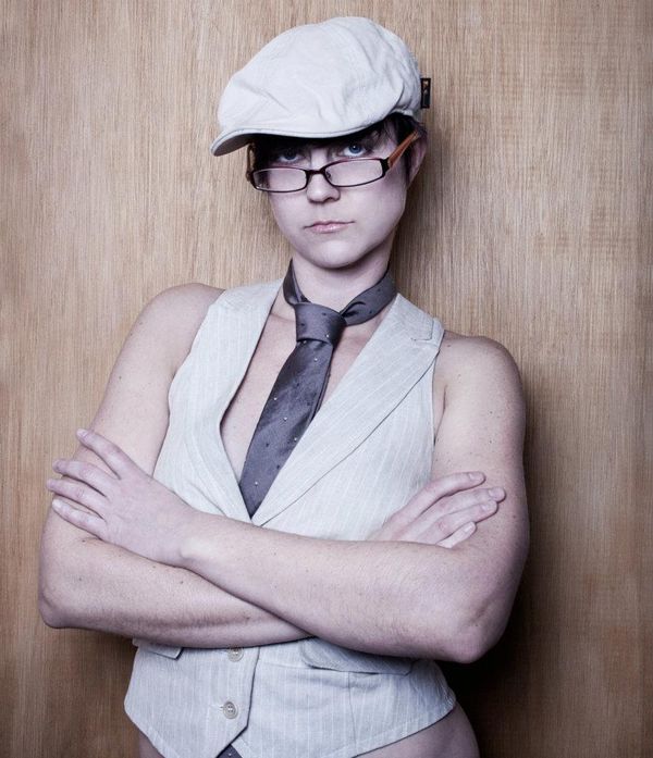 Studio portrait of Jen Woolfe in a newsboy cap, white vest and tie, arms crossed