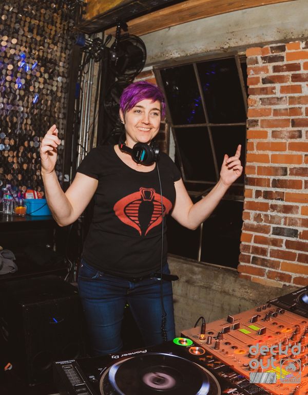 Jen Woolfe dancing behind the decks in front of a brick wall